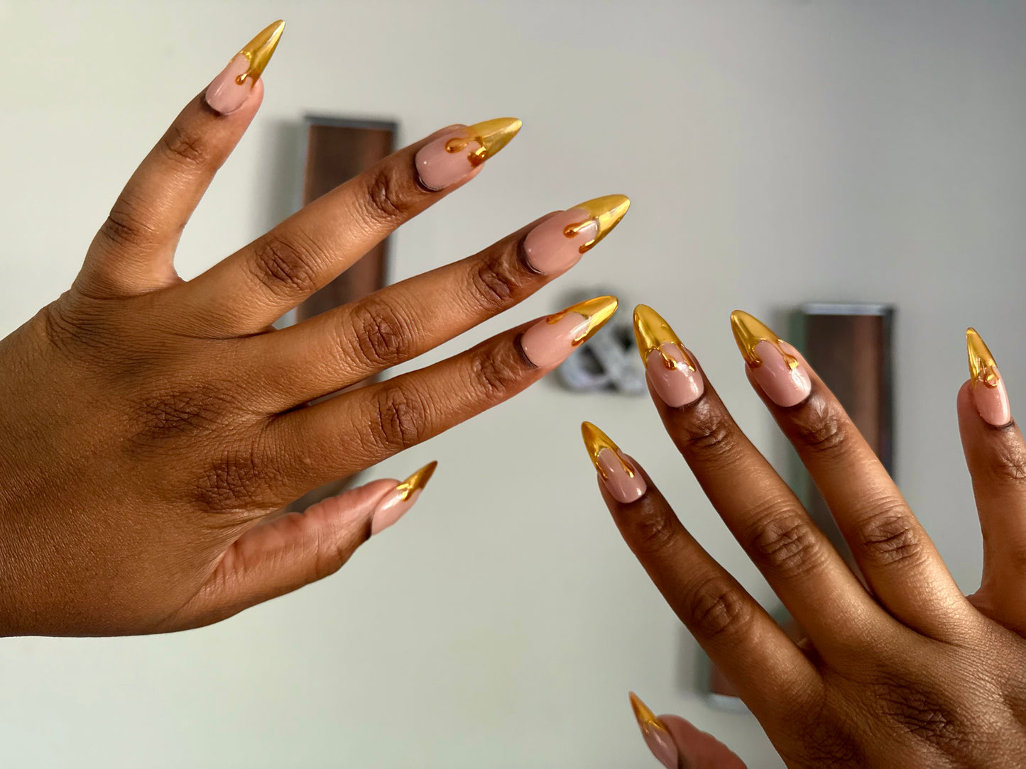 Close-up of two hands with gold nail polish on a neutral background
